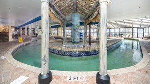 Ein Poolbereich im Innenbereich mit einer zentralen Wasserspielen, einer strohgedeckten Struktur und einer gefliesten Kante.