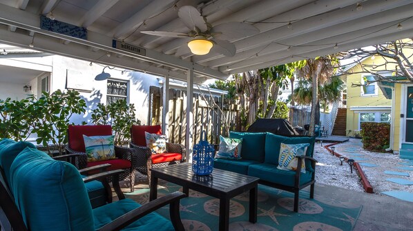 A covered outdoor seating area with a ceiling fan, a table, and chairs with cushions.