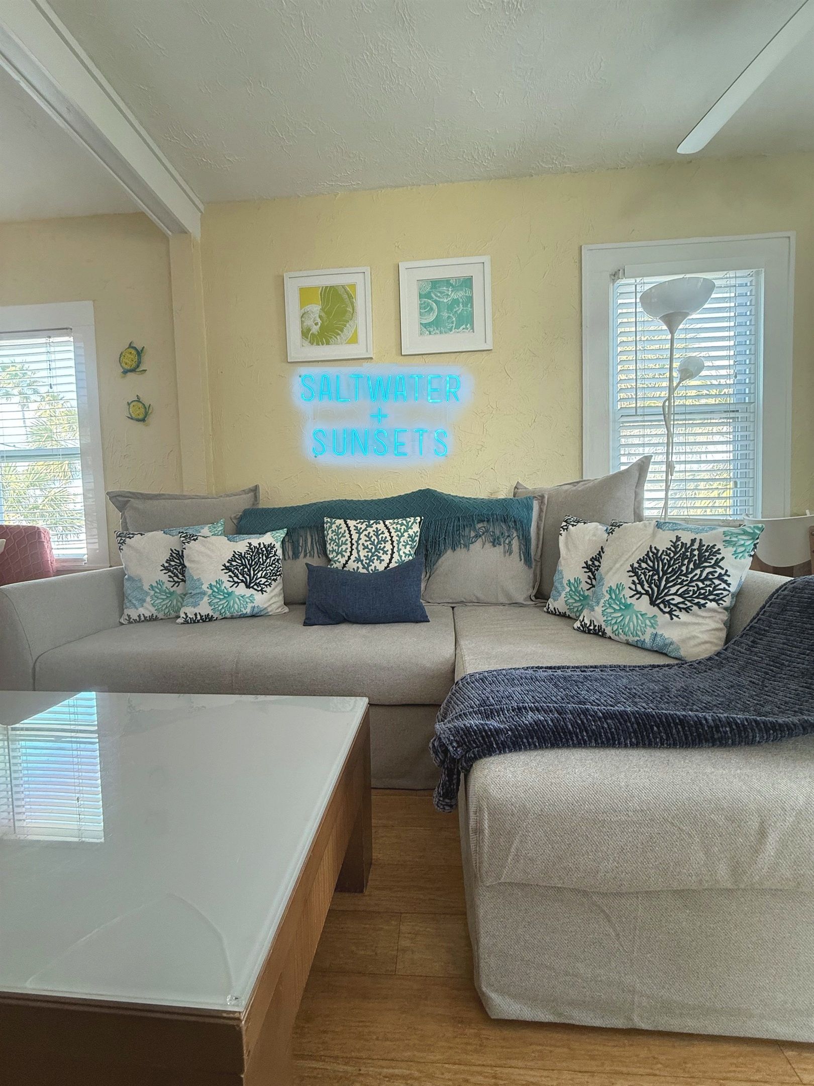 A living room with a sofa, two armchairs, a coffee table, and a wall-mounted neon sign.