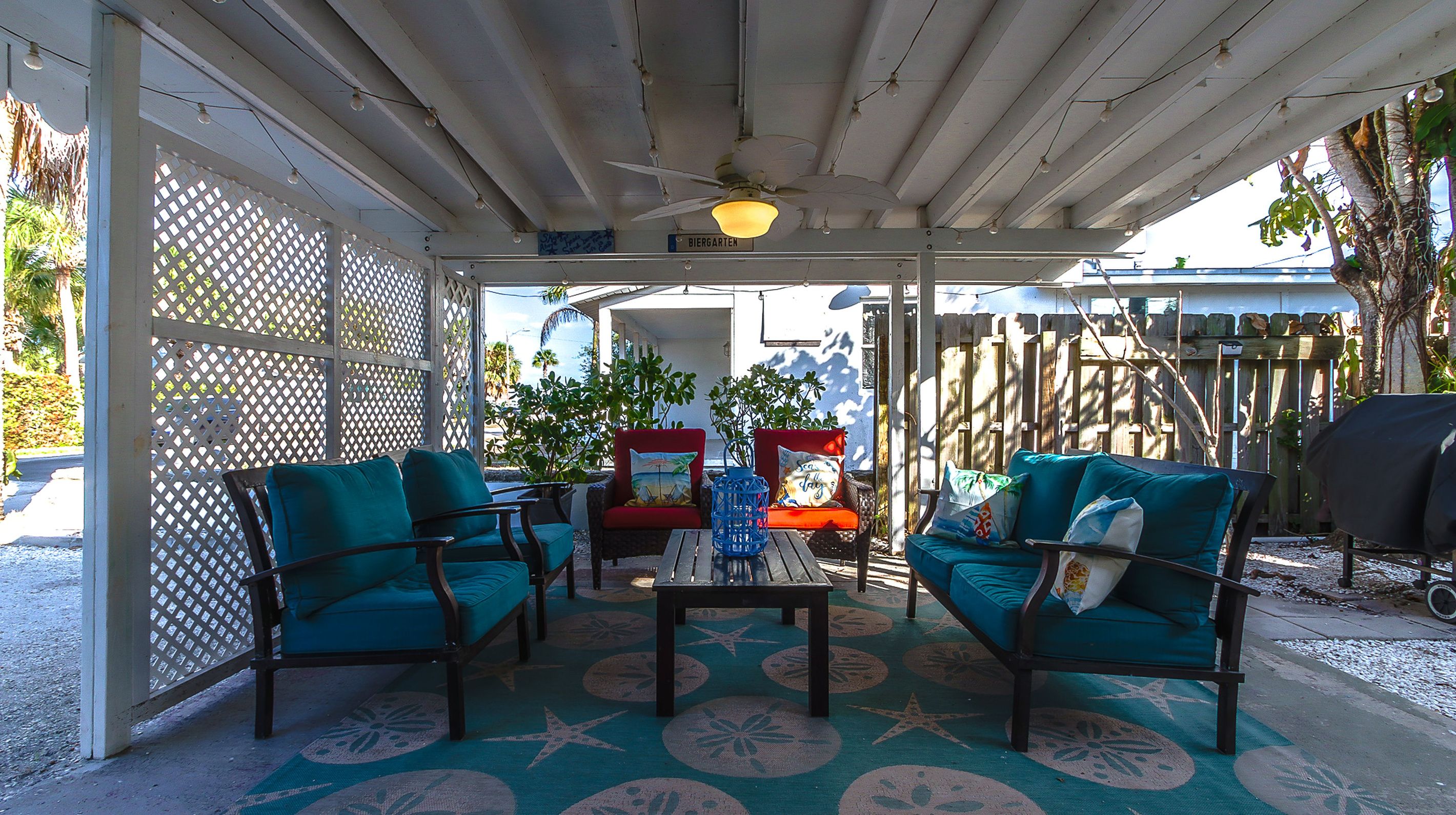 An outdoor patio with two teal sofas, a wooden table, and a ceiling fan.