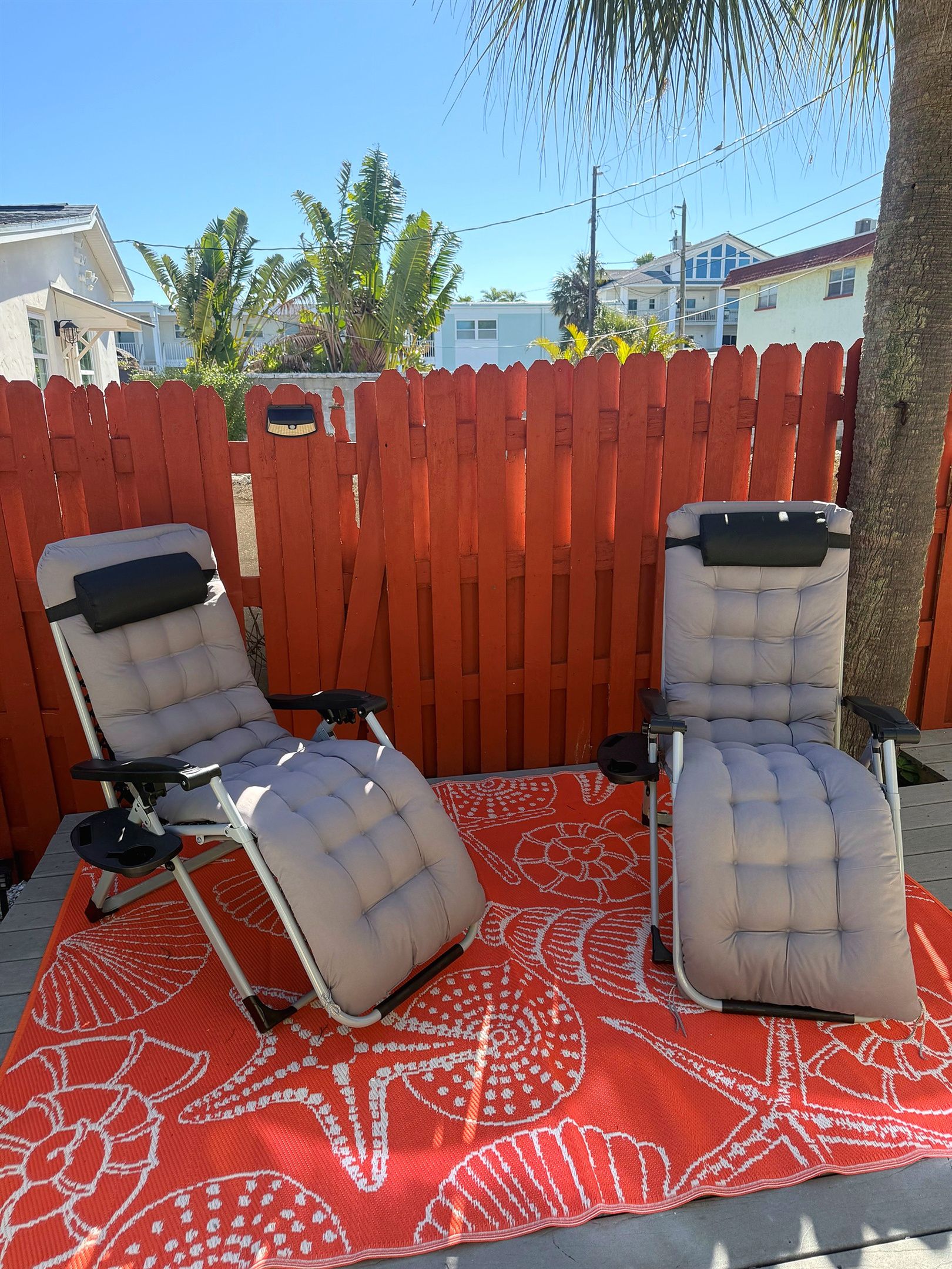 Twee loungestoelen met voetbankjes op een kamerkleed, voor een houten hek.