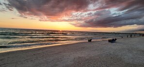 A beach with a sunset, waves, and people fishing.