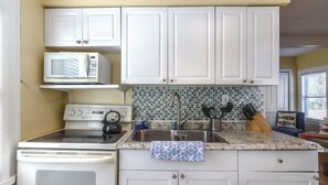 A kitchen with white cabinets, a microwave, a stove, a sink, and a tiled backsplash.