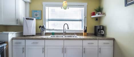 A kitchen with a built-in dishwasher, a stainless steel sink, and a window with blinds.