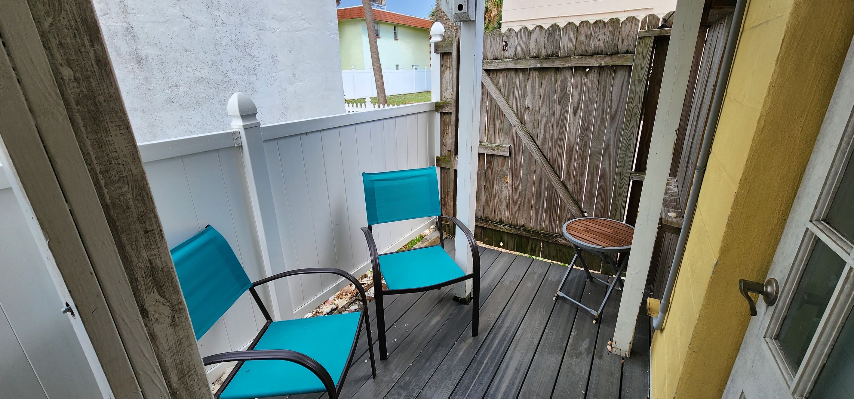 Un pequeño espacio al aire libre con dos sillas y una mesa, rodeado por una valla de madera y una pared blanca.