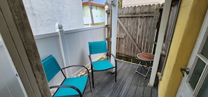 Un pequeño espacio al aire libre con dos sillas y una mesa, rodeado por una valla de madera y una pared blanca.