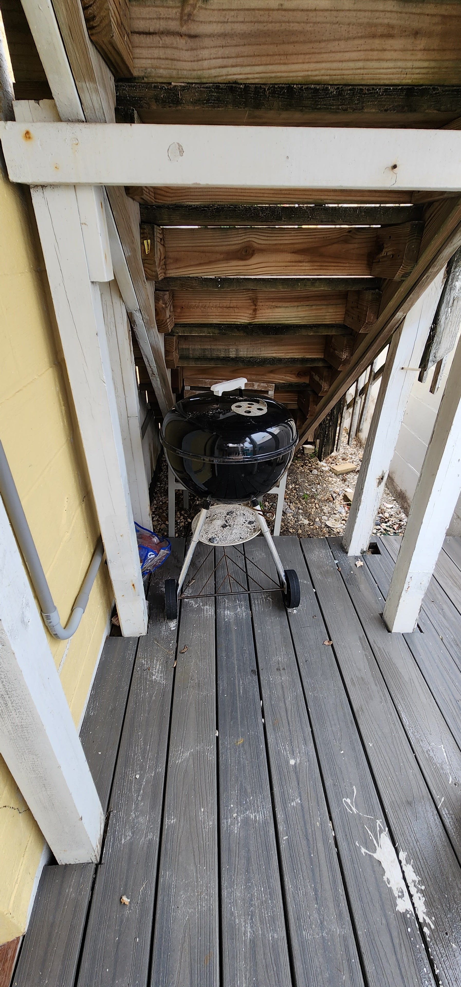 A wooden deck with a barbecue grill underneath a wooden structure.