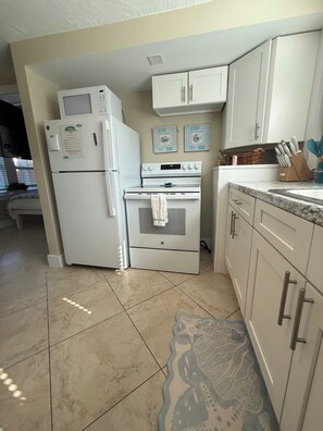 A kitchen with white appliances, including a refrigerator, oven, and microwave. There are cabinets and a countertop with a knife block.