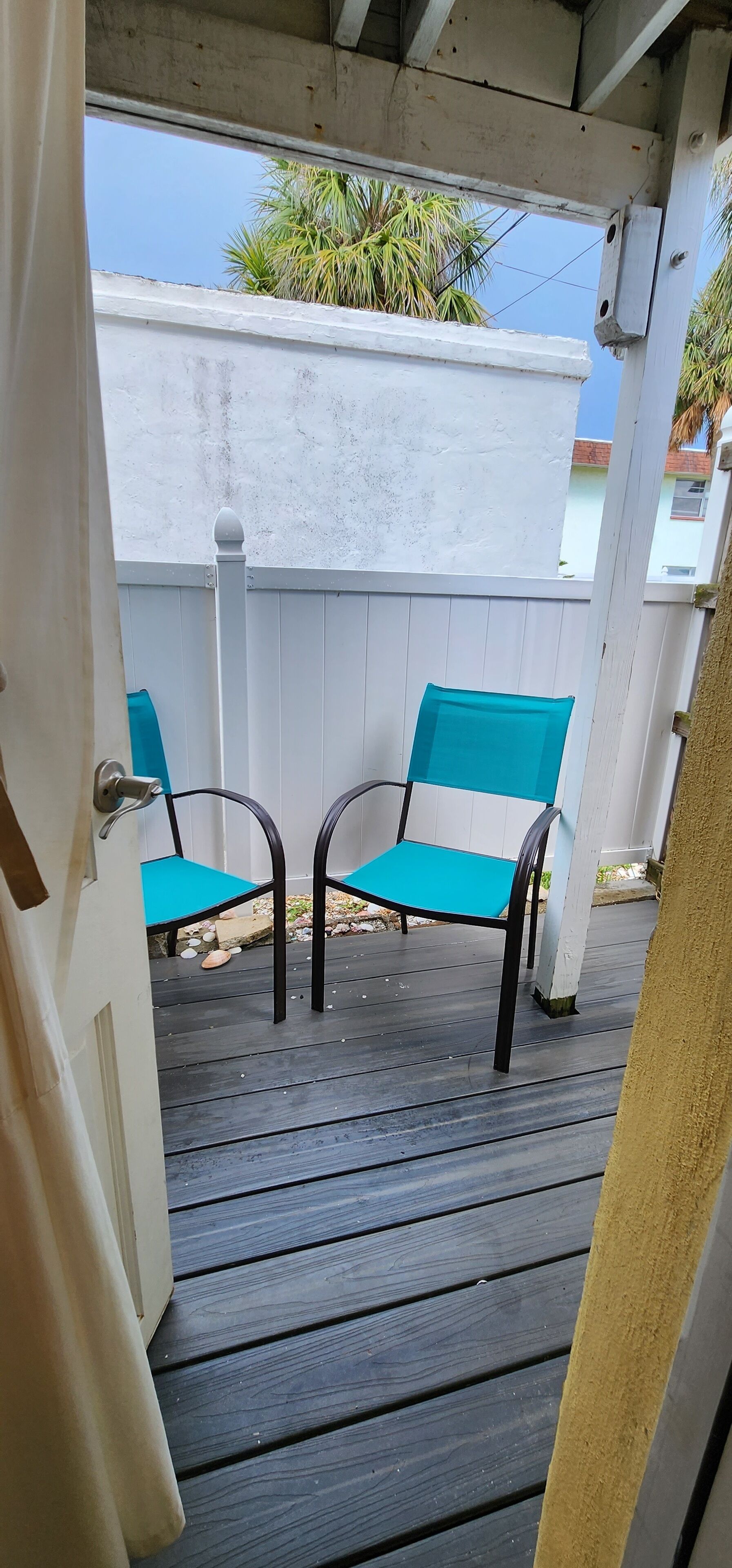 Une terrasse couverte avec deux chaises turquoise et une clôture blanche.