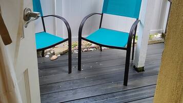Une terrasse couverte avec deux chaises turquoise et une clôture blanche.