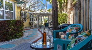 Un patio con mobiliario exterior, una mesa con una botella y un vaso, y un área de estar cubierta.
