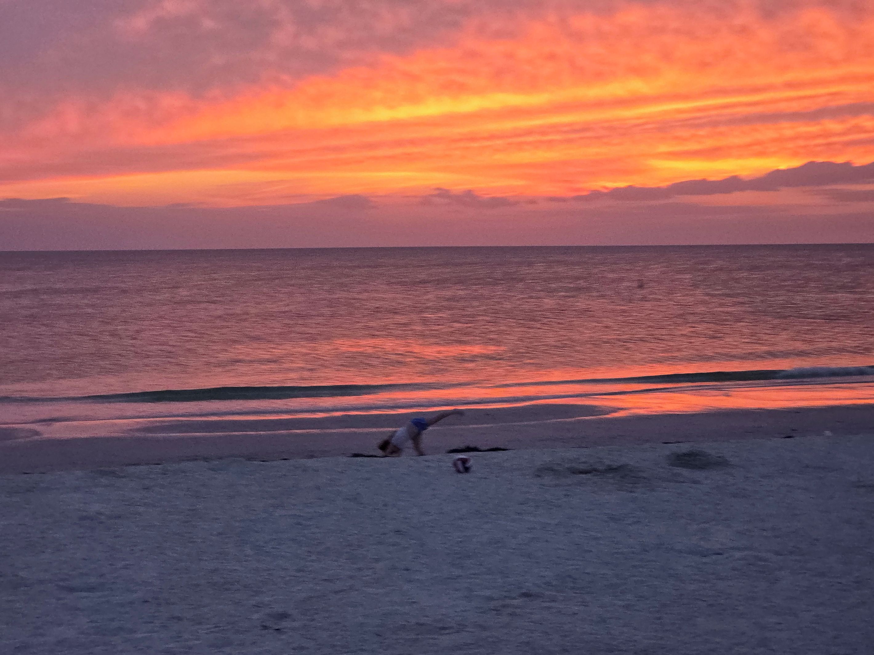 Une plage au coucher du soleil, avec des vagues et une personne dans l’eau.