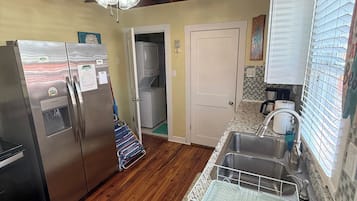 A kitchen with a stainless steel refrigerator, a built-in oven, a granite countertop, a sink with a dish rack, and a ceiling fan.