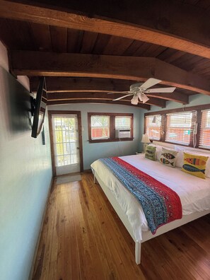 Une chambre avec un plafond en bois, un lit recouvert d’une couverture colorée et un ventilateur de plafond.