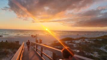 A sunset view from a boardwalk with people walking, a beach in the background, and a cloudy sky.
