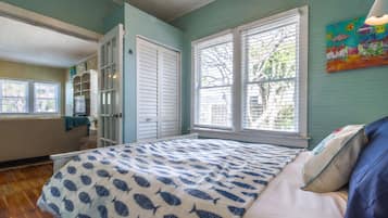 A bedroom with a bed, a window with blinds, a door, and a painting on the wall.