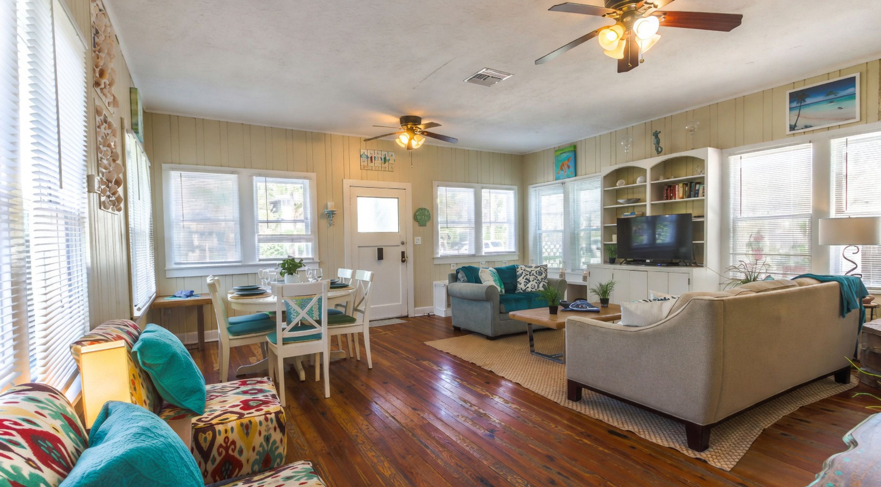 A spacious living area with a dining table, two sofas, a TV, and a ceiling fan.