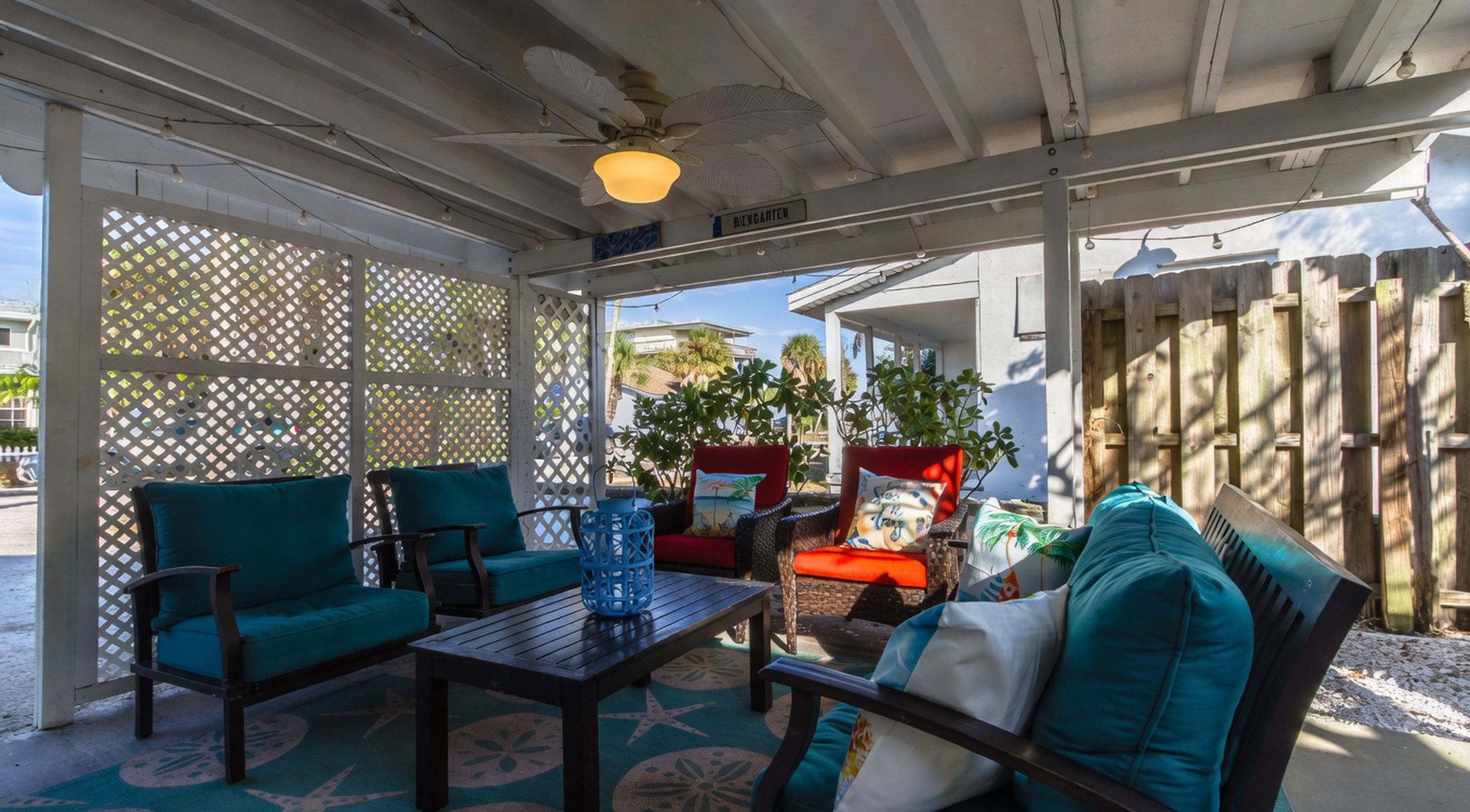 A covered outdoor seating area with chairs and a table, a wooden fence, and a view of a residential street.