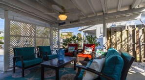 A covered outdoor seating area with chairs and a table, a wooden fence, and a view of a residential street.