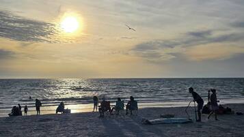 A beach scene with people and a boat, sun setting in the background.