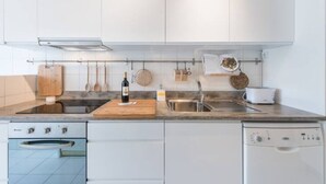 Eine moderne Küche mit weißen Schränken, einer Spüle aus Edelstahl, einem Holztisch zum Schneiden und einer Weinflasche.