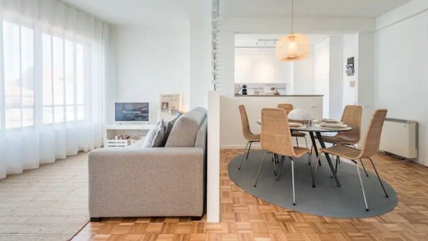 Ein modernes Wohnzimmer mit Sofa, Essbereich mit Tisch und Stühlen sowie K üche im Hintergrund.