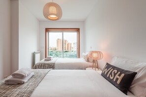 Une chambre d’hôtel avec deux lits, une grande fenêtre donnant sur la ville, un radiateur et une lampe sur la table de chevet.