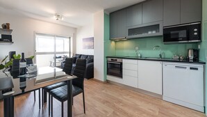 A modern kitchen with grey cabinets, a Bosch microwave, and a dishwasher. There is a dining area with a glass table and black chairs.