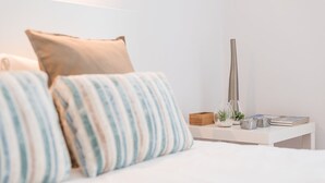 Een keurig opgemaakt bed met gestreepte kussens, een nachtkastje met een vaas, boeken en decoratieve objecten.