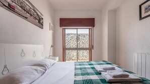 A bedroom with a bed, a window with a view, a radiator, and a wall with a light bulb drawing. - GuestReady - Urban escape with a view (Porto)