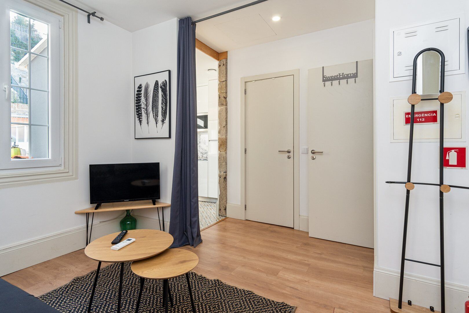 Una habitación moderna con televisor de pantalla plana, una mesita redonda pequeña, una alfombra estampada y una puerta con un letrero que dice 'Sweet Home'.