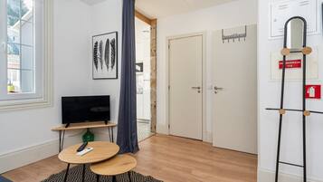 Una habitación moderna con televisor de pantalla plana, una mesita redonda pequeña, una alfombra estampada y una puerta con un letrero que dice 'Sweet Home'.