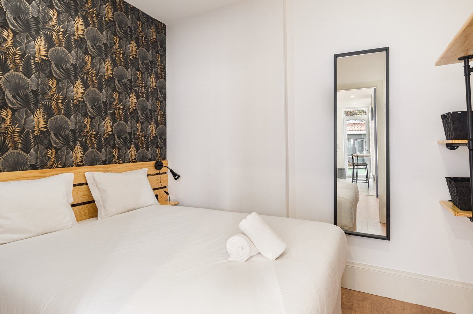 Habitación de hotel con una cama, un espejo grande y una pared con diseño de hojas.