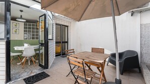 An outdoor patio with a wooden table and chairs, a black chair, and a large umbrella. - GuestReady - Porto by Pilar Ridge (Vila Nova de Gaia)