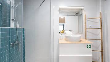 Ein modernes Badezimmer mit Duschkabine aus Glas, einem weißen Waschbecken mit Holzablage und einem Spiegel darüber.