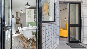 A modern kitchen with white cabinets, a dining area with a round table and chairs, and a yellow chair outside. - GuestReady - Porto by Pilar Ridge (Vila Nova de Gaia)