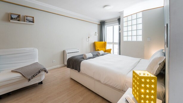 A hotel room with a bed, a sofa, a chair, a bedside table with a lamp, and a window with curtains. - GuestReady - Porto by Pilar Ridge (Vila Nova de Gaia)