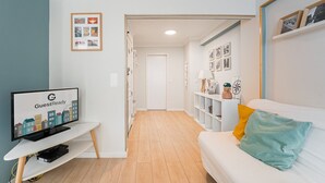 A modern living room with a white sofa, a TV on a stand, and a hallway leading to a door. - GuestReady - Porto by Pilar Ridge (Vila Nova de Gaia)