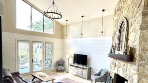 Un salón amplio con chimenea de piedra, un sofá de cuero, un televisor y un comedor con mesa y sillas.