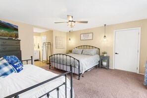 A bedroom with a bed, a dresser, a ceiling fan, a bedside table, and a door.