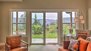 A spacious living room with a large sliding glass door leading to a garden. There is a leather armchair and a sofa with cushions.
