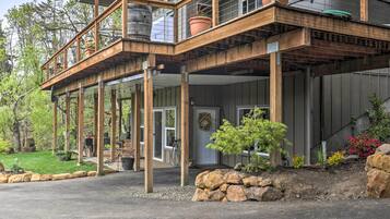 A two-story wooden house with a balcony, a garage door, and a garden with rocks and plants.