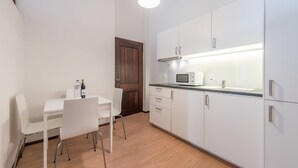 A compact kitchen with white cabinets, a microwave, and a dining area with a white table and chairs.