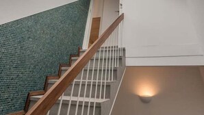 A staircase with a wooden handrail leading to a room with a skylight and a green-tiled wall.