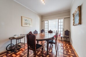 A dining area with a wooden table and chairs, a small side table with a pitcher, and a painting on the wall.