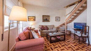 A living room with a sofa, armchair, coffee table, and a TV. There is a staircase with a wooden railing. - GuestReady - Urban escape in Porto (Porto)