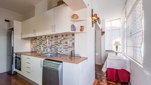A compact kitchen with white cabinets, a tiled backsplash, and a dishwasher. - GuestReady - Urban escape in Porto (Porto)