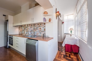 Una cucina compatta con mobili bianchi, zoccolo in piastrelle e lavastoviglie.