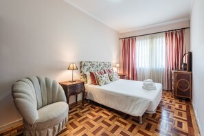 A hotel room with a bed, a chair, a nightstand, a lamp, a TV, and a wooden parquet floor.