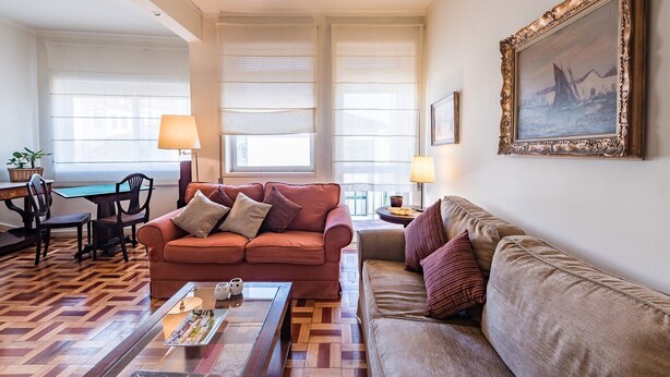 A living room with a brown sofa, a glass coffee table, and a dining area with a wooden table and chairs. - GuestReady - Urban escape in Porto (Porto)